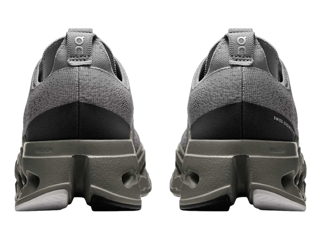 Tenis deportivos On Cloud color gris con suela gruesa perforada y logotipo rosa.