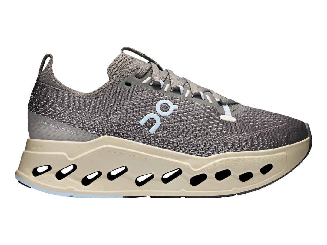 Tenis deportivos On Cloudsurf Max color gris asfalto con suela gruesa beige y detalles en azul claro.