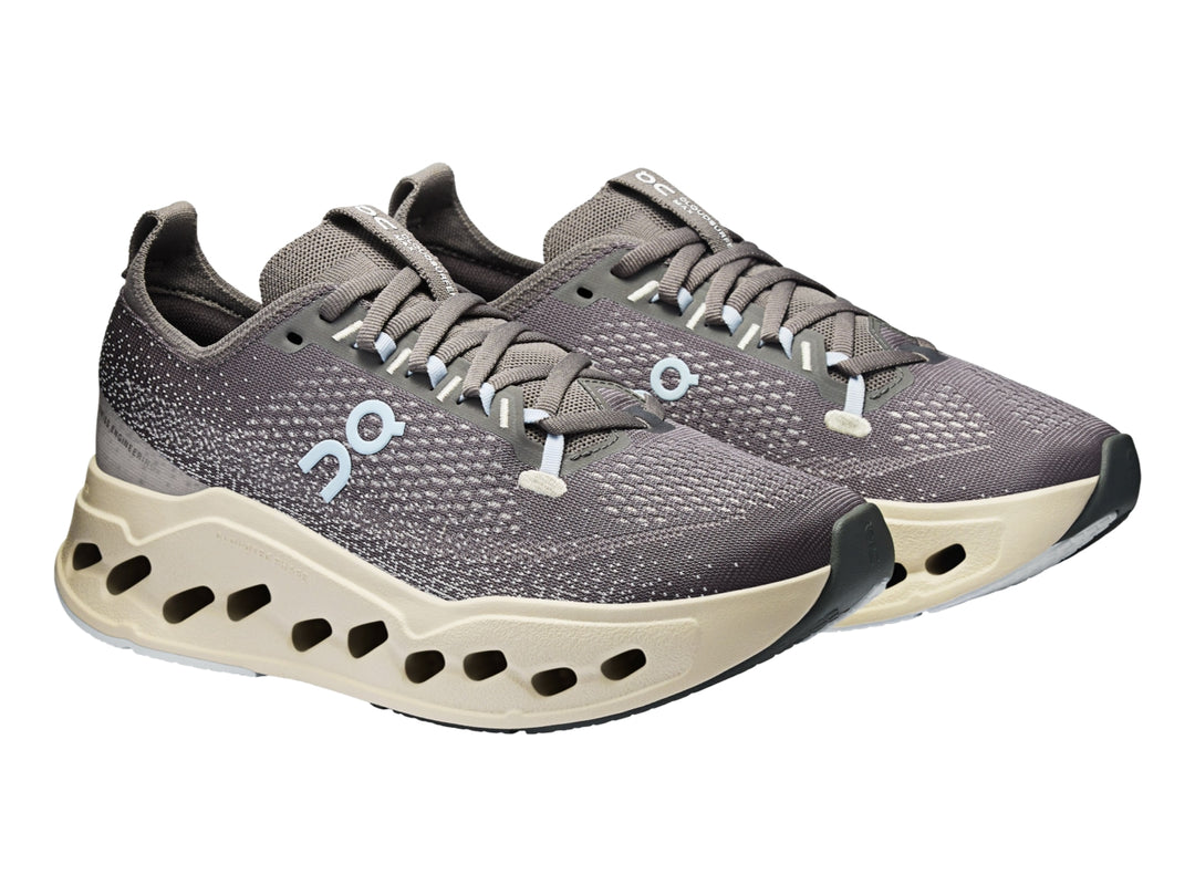 Tenis deportivos On Cloudsurf Max color gris asfalto con suela gruesa beige y detalles en azul claro.