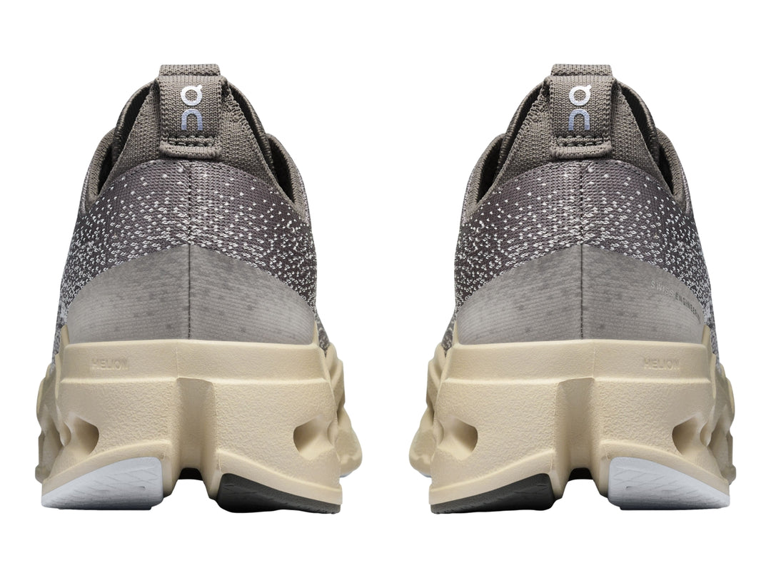 Tenis deportivos On Cloudsurf Max color gris asfalto con suela gruesa beige y detalles en azul claro.