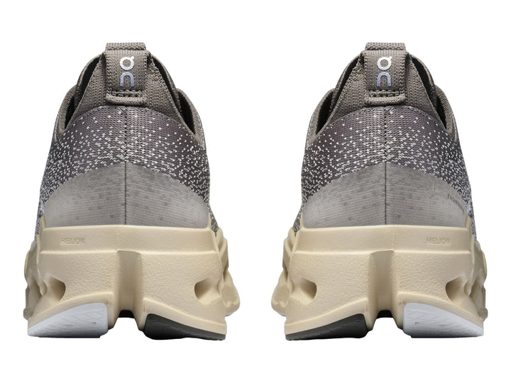 Tenis deportivos On Cloudsurf Max color gris asfalto con suela gruesa beige y detalles en azul claro.