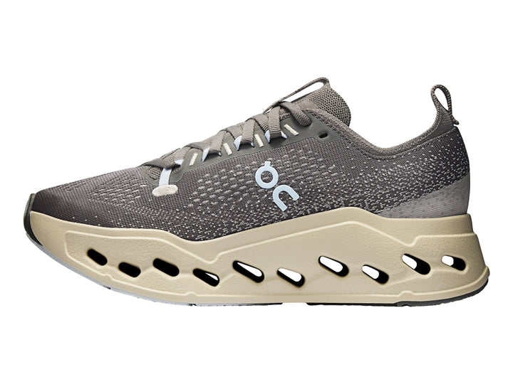 Tenis deportivos On Cloudsurf Max color gris asfalto con suela gruesa beige y detalles en azul claro.