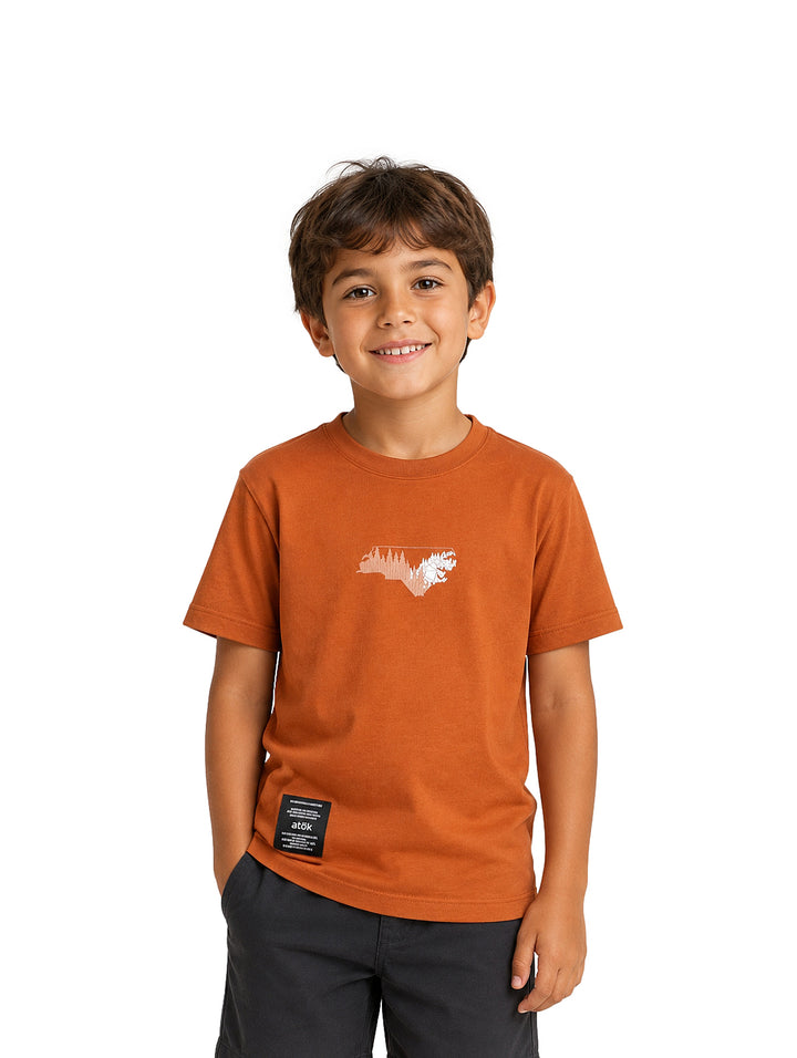 Niño usando camiseta color camel con estampado blanco y etiqueta negra.
