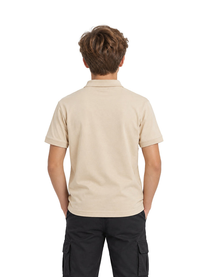 Niño vistiendo playera polo color arena de marca ATOK con cierre en el cuello y pantalones negros.