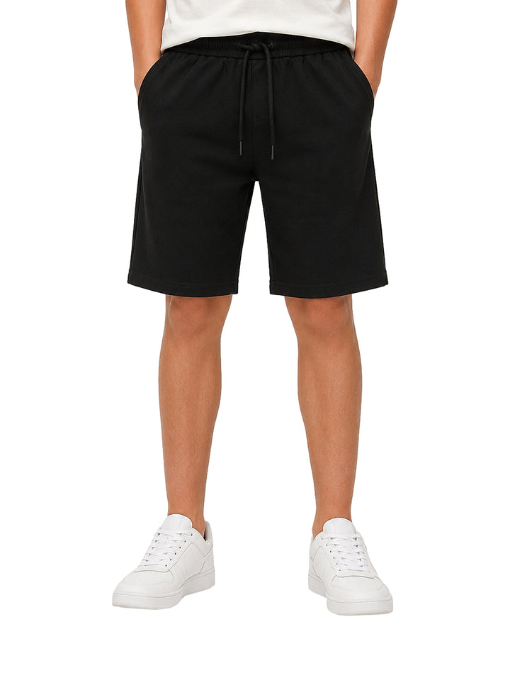 Niño vistiendo bermuda color negro con cintura elástica y cordón, acompañada de tenis blancos.