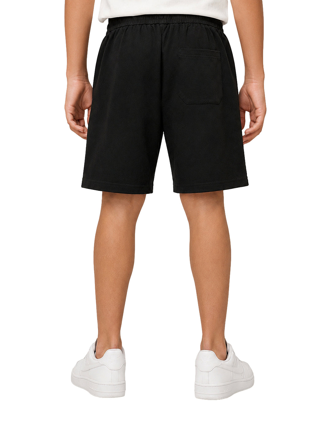 Niño vistiendo bermuda color negro con cintura elástica y cordón, acompañada de tenis blancos.