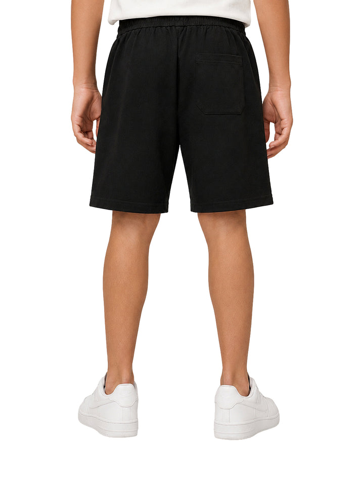 Niño vistiendo bermuda color negro con cintura elástica y cordón, acompañada de tenis blancos.