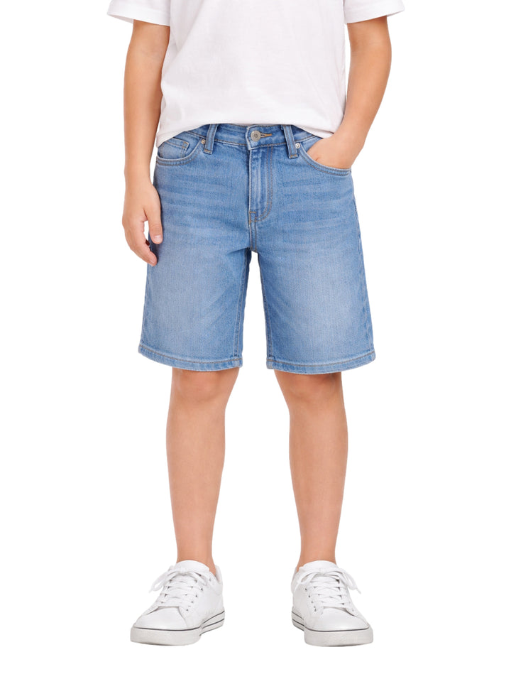 Niño vistiendo bermuda de mezclilla color azul claro y tenis blancos sobre fondo blanco.