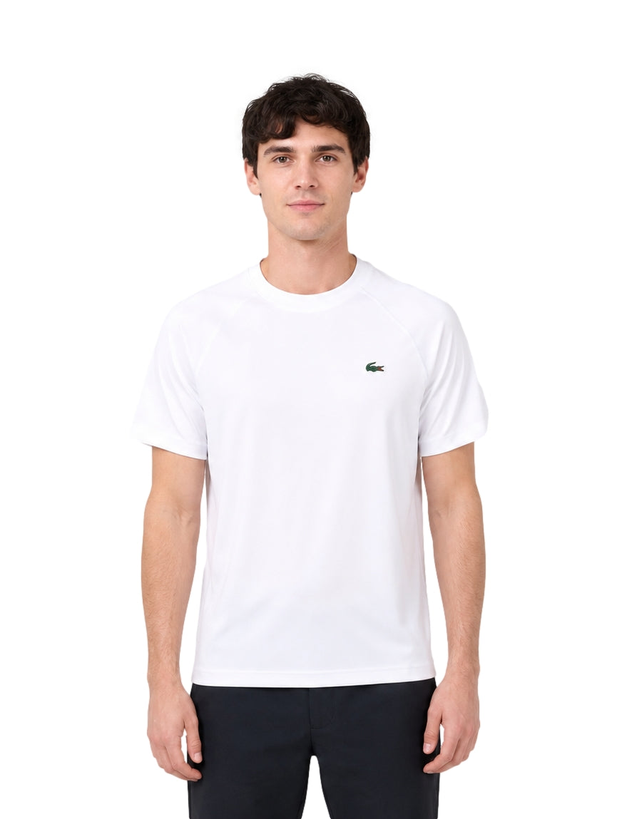 Hombre vistiendo una playera blanca de manga corta de la marca Lacoste con logo en el pecho.