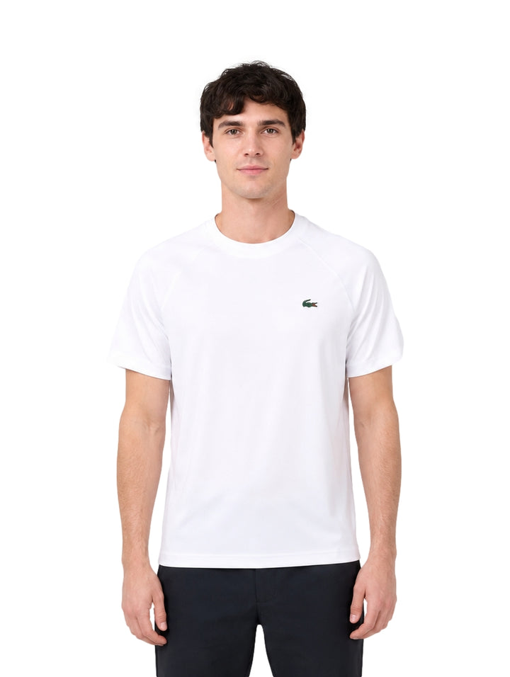 Hombre vistiendo una playera blanca de manga corta de la marca Lacoste con logo en el pecho.