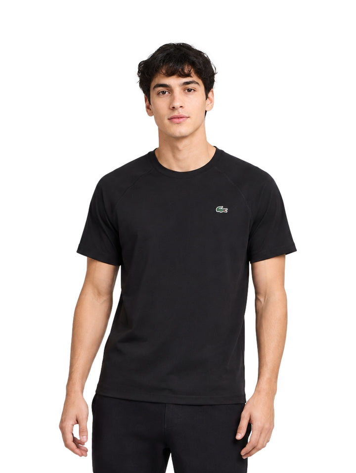 Hombre vistiendo una playera Lacoste de color negro con manga corta y cuello redondo.