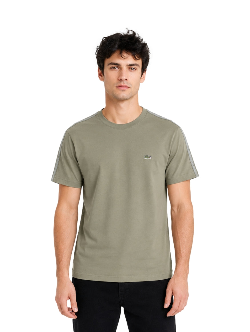 Hombre vistiendo playera Lacoste color khaki con detalles grises en los hombros y cuello redondo.