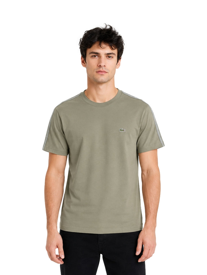 Hombre vistiendo playera Lacoste color khaki con detalles grises en los hombros y cuello redondo.