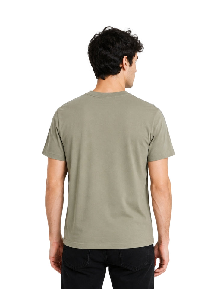 Hombre vistiendo playera Lacoste color khaki con detalles grises en los hombros y cuello redondo.