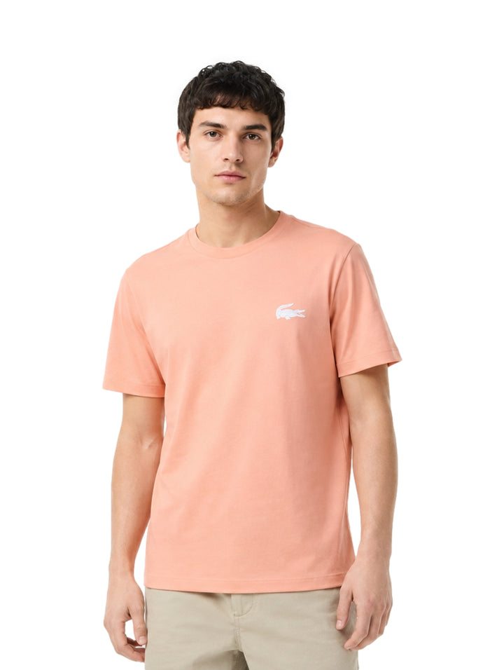 Hombre vistiendo una playera Lacoste de color salmón con cuello redondo y manga corta.