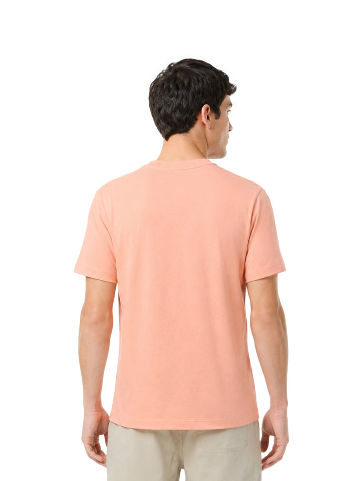 Hombre vistiendo una playera Lacoste de color salmón con cuello redondo y manga corta.