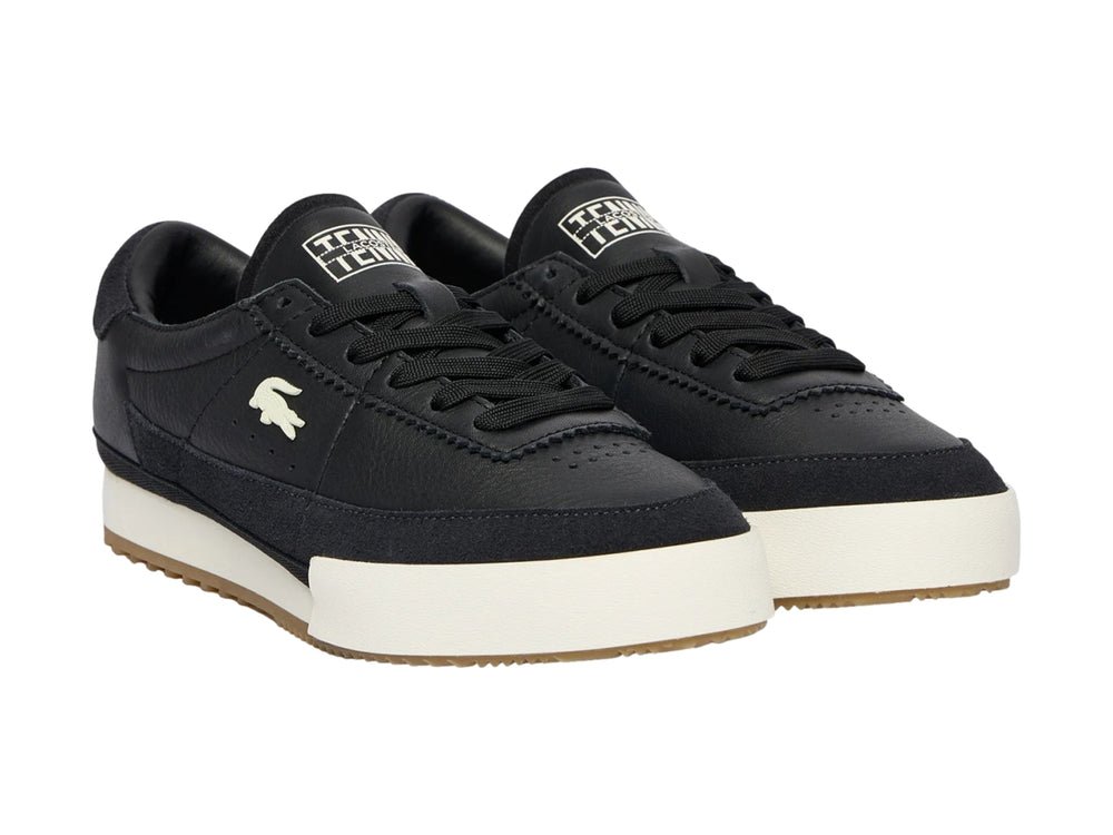 Tenis Lacoste de cuero negro con suela blanca y base de goma marrón.