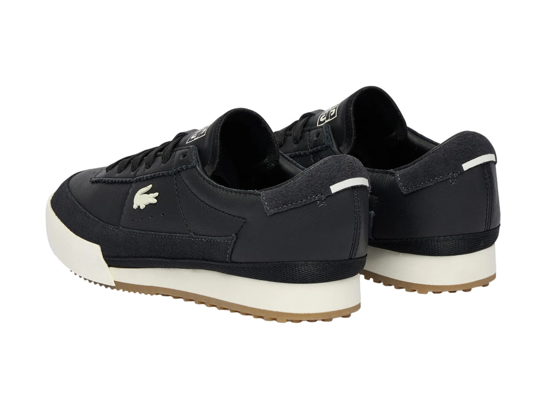 Tenis Lacoste de cuero negro con suela blanca y base de goma marrón.