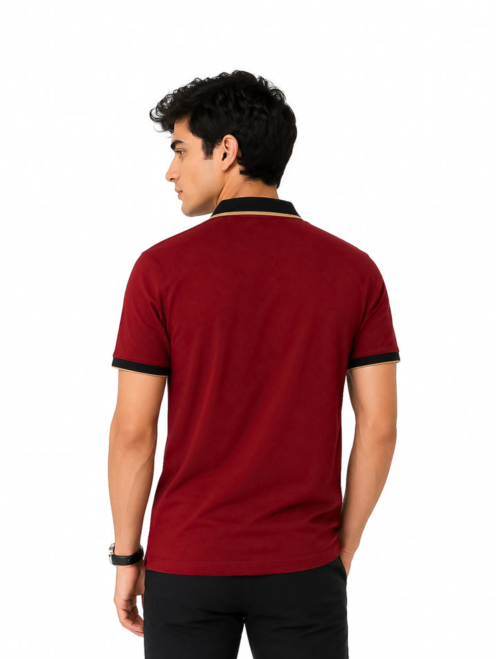 Hombre vistiendo playera polo color burgundy con detalles negros y dorados en el cuello.