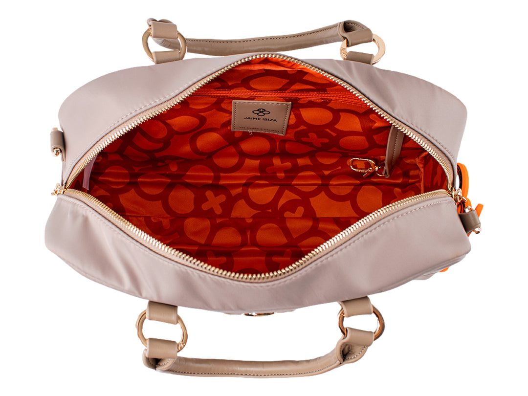 Bolsa de mano color taupe con asa superior, detalles dorados y un accesorio colgante color naranja.