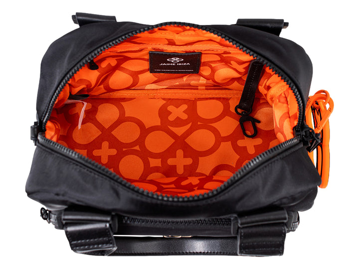 Bolsa negra Jaime Ibiza con asa superior y accesorio circular decorativo color naranja.
