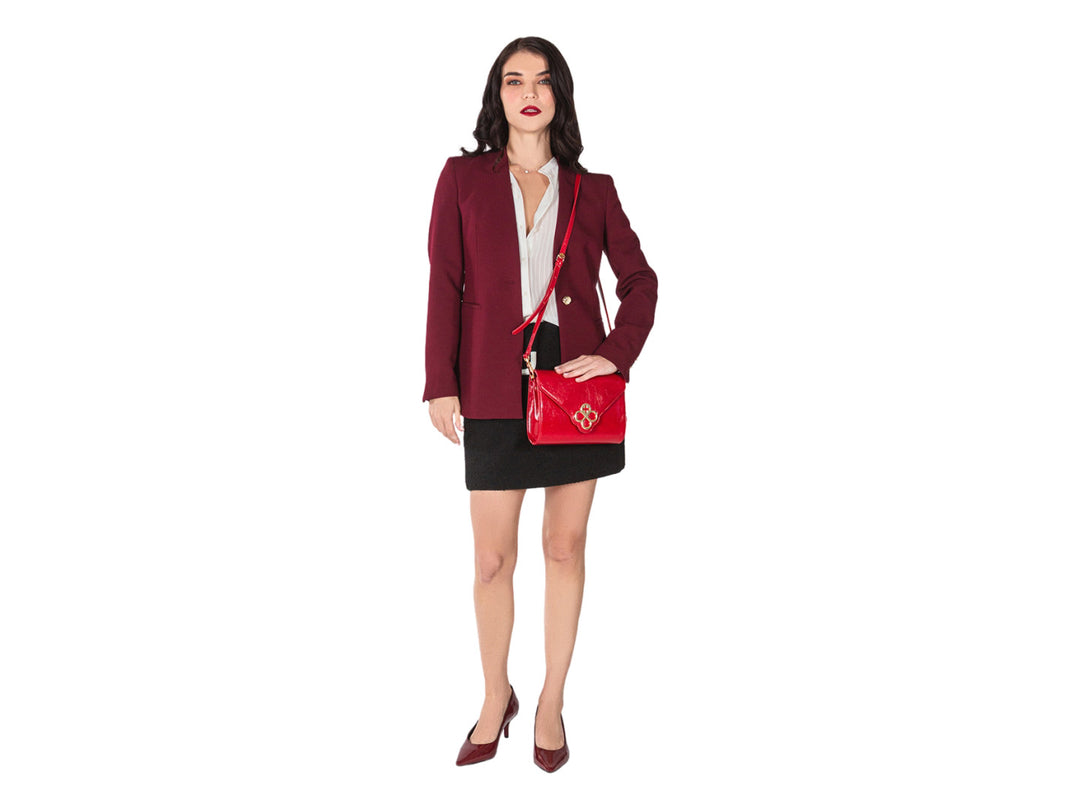 Bolsa roja de cuero con herraje dorado central y correa ajustable.