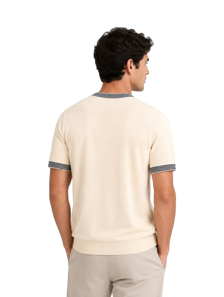 Hombre vistiendo playera tejida color arena con detalles de rayas oscuras en el cuello y los puños de las mangas.