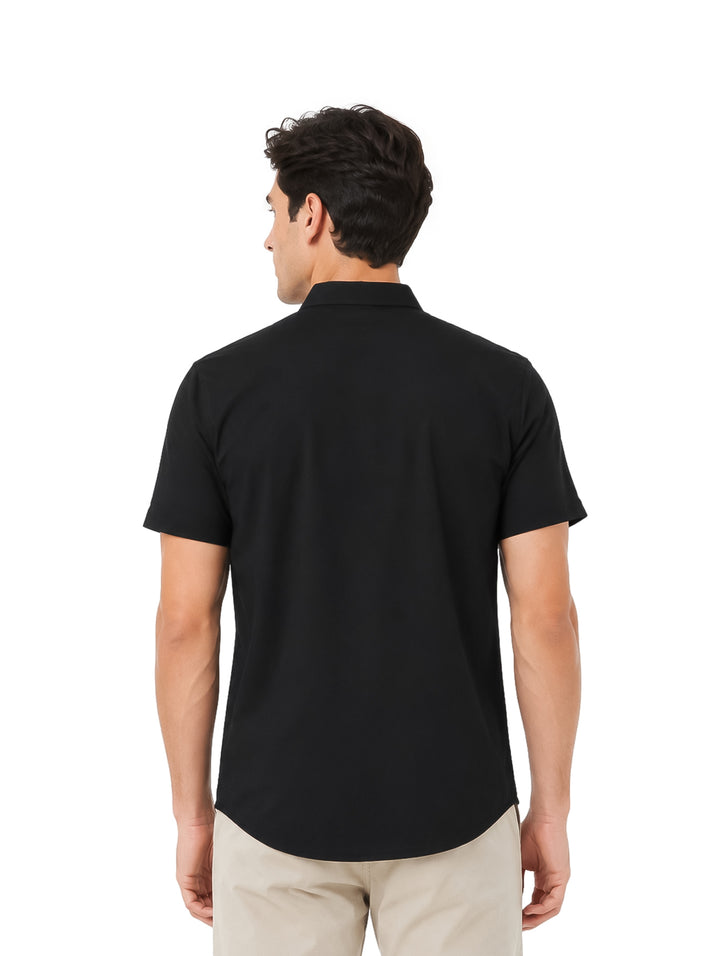Hombre vistiendo una camisa negra de manga corta y pantalones beige sobre fondo blanco.