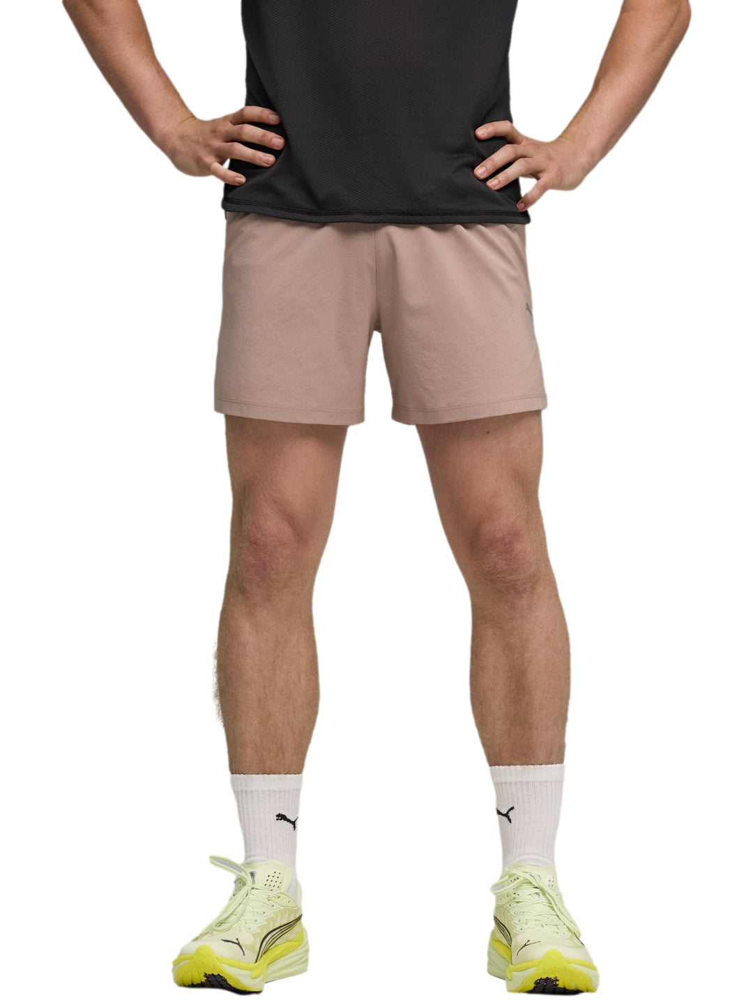 Hombre vistiendo shorts deportivos PUMA color sandstone con camiseta negra y tenis amarillos.