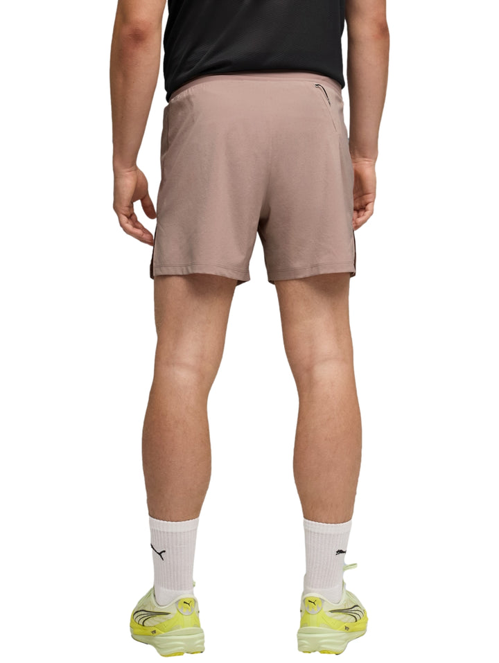 Hombre vistiendo shorts deportivos PUMA color sandstone con camiseta negra y tenis amarillos.