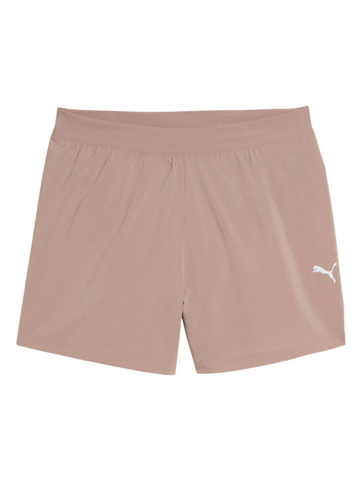 Hombre vistiendo shorts deportivos PUMA color sandstone con camiseta negra y tenis amarillos.