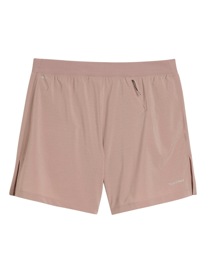 Hombre vistiendo shorts deportivos PUMA color sandstone con camiseta negra y tenis amarillos.