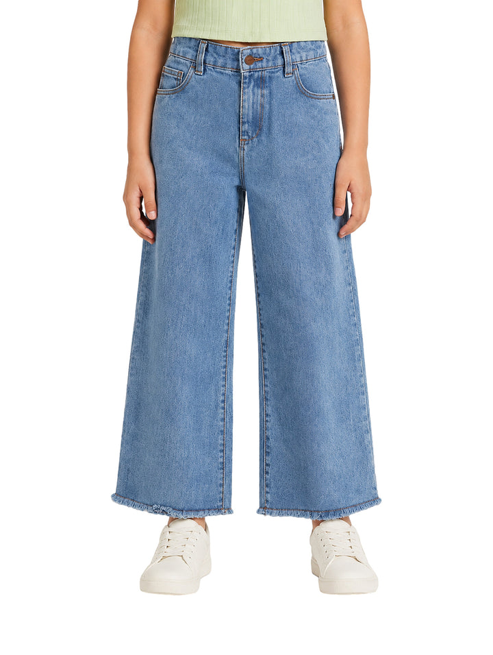Jeans azules de pierna ancha para niña con bajos deshilachados.