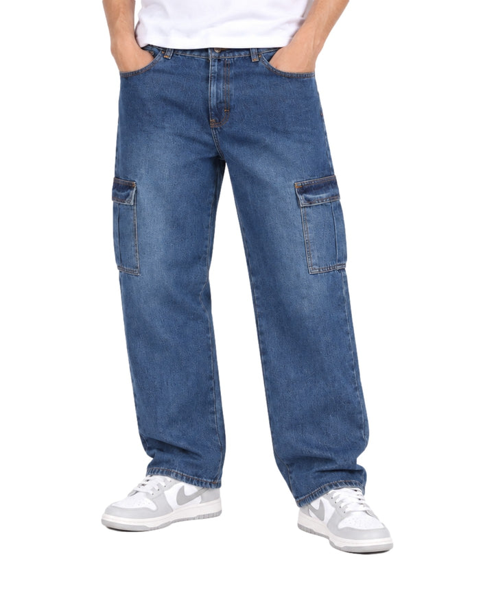 Hombre vistiendo jeans baggy color azul stone con bolsillos cargo laterales y tenis blancos.