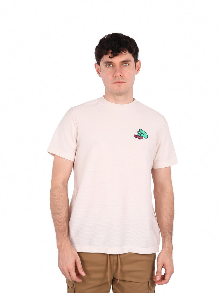 Hombre vistiendo playera de manga corta color hueso con un pequeño estampado en el pecho.