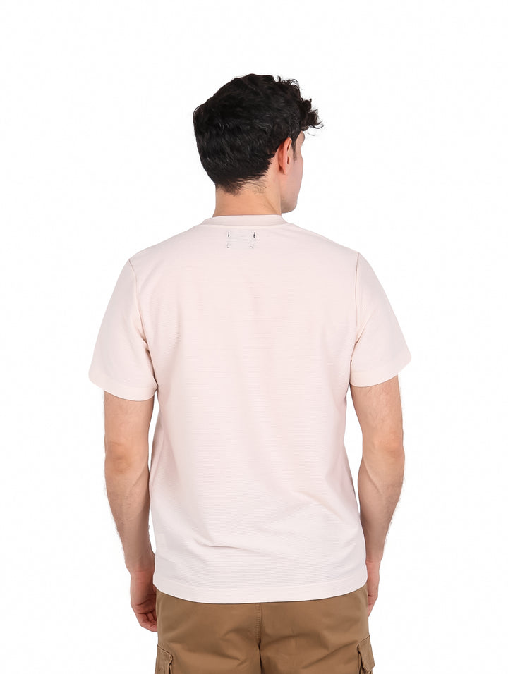 Hombre vistiendo playera de manga corta color hueso con un pequeño estampado en el pecho.