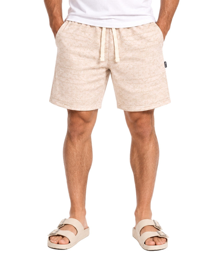 Hombre vistiendo short Action Gear estampado en color hueso con cordón ajustable y sandalias claras.