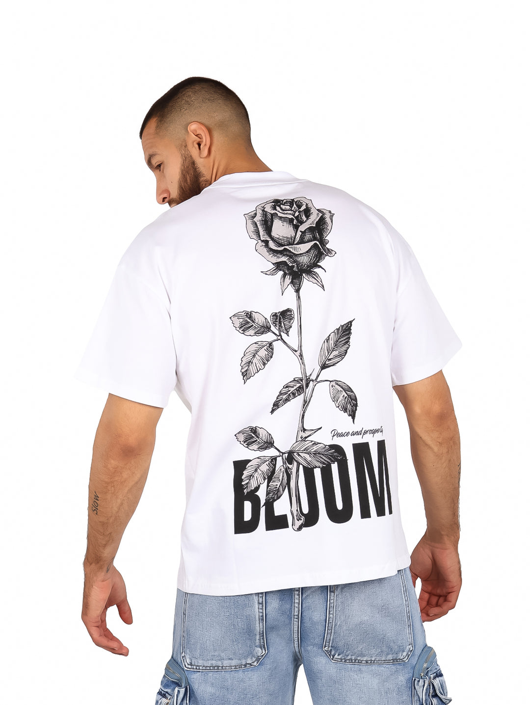 Hombre vistiendo una playera blanca de manga corta con estampado negro en el pecho que dice BLOOM.