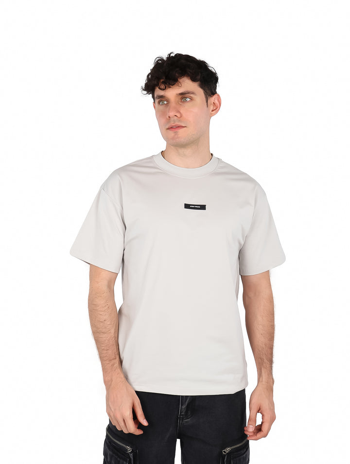 Hombre vistiendo una playera de manga corta color gris con cuello redondo y un pequeño detalle rectangular en el pecho.