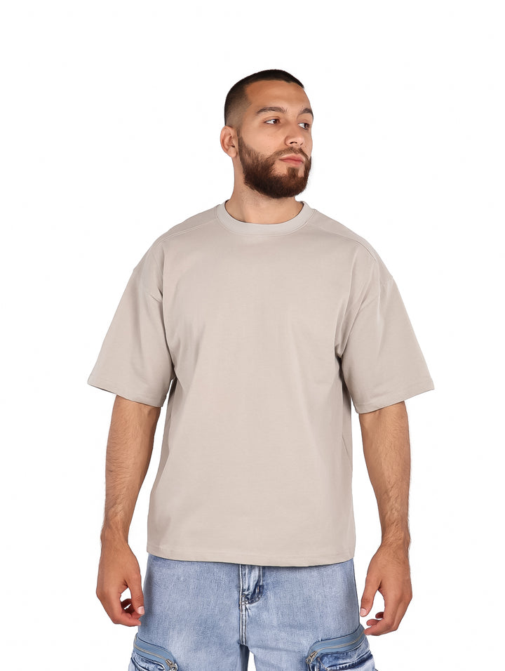 Hombre vistiendo una playera de manga corta color gris claro de corte amplio y cuello redondo.