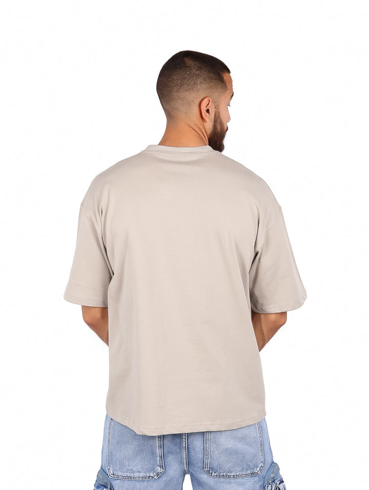 Hombre vistiendo una playera de manga corta color gris claro de corte amplio y cuello redondo.