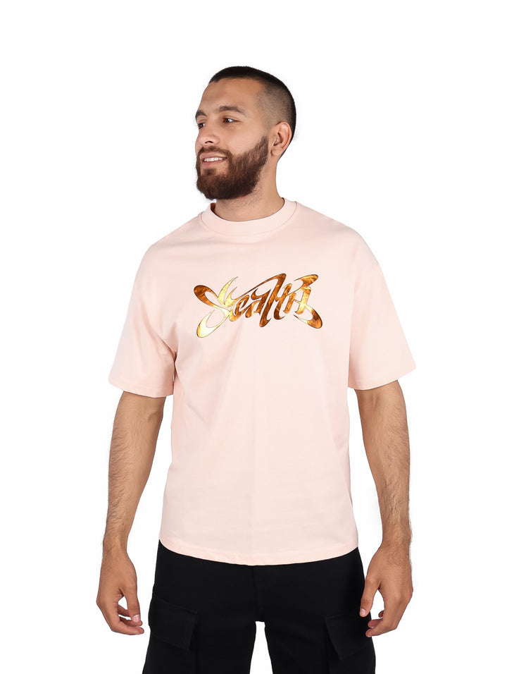Hombre vistiendo una playera color rosa de manga corta con un gráfico dorado en el pecho.