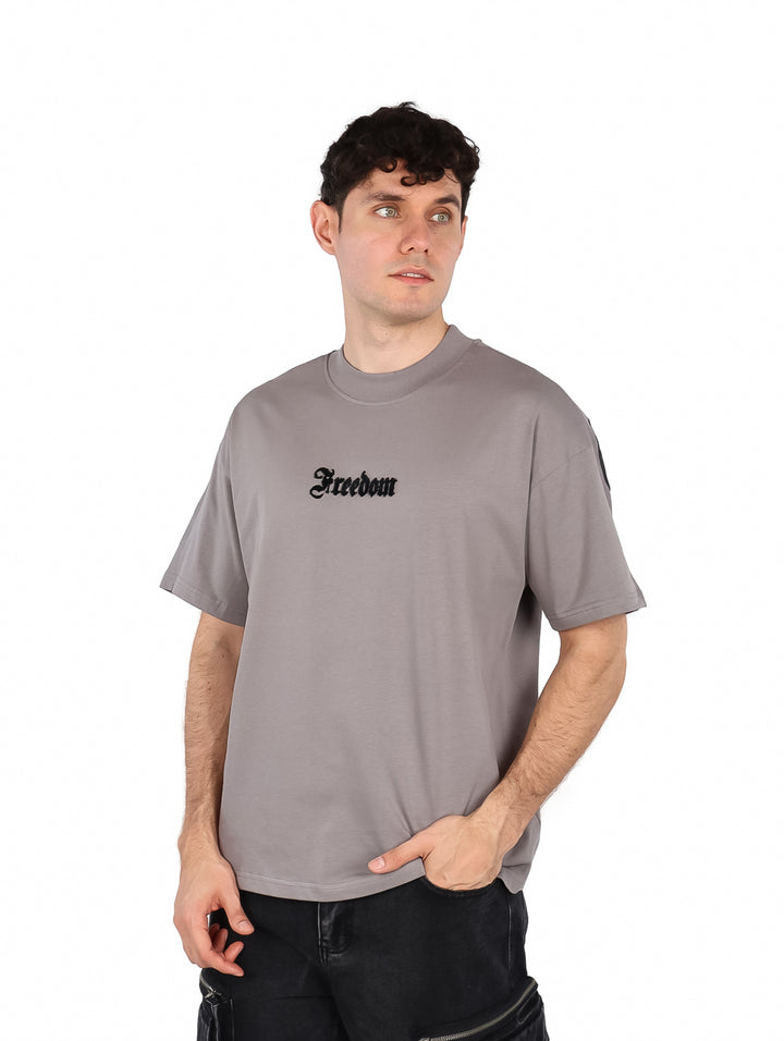 Hombre vistiendo playera color gris de manga corta con la palabra Freedom en el pecho.