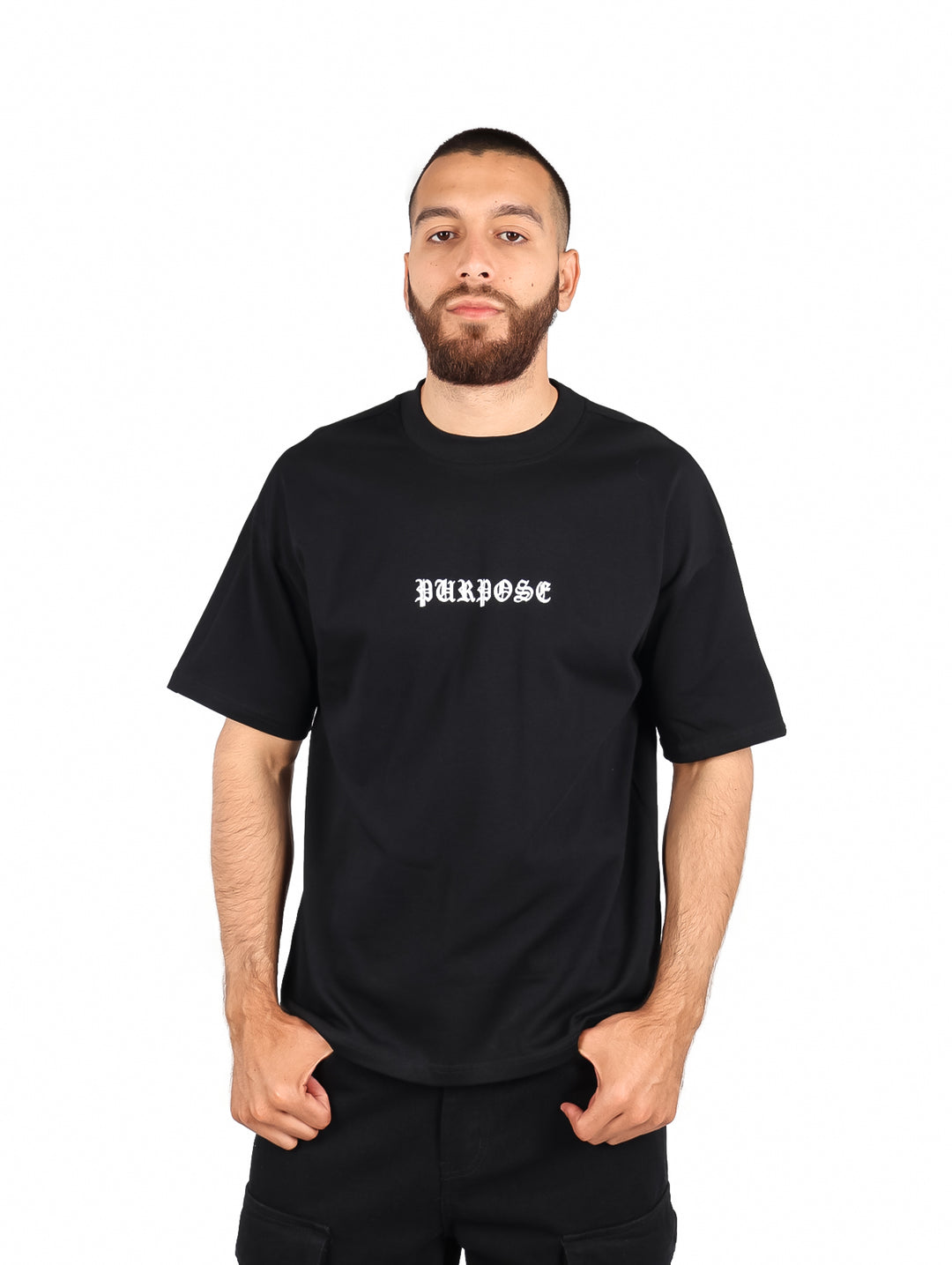 Hombre vistiendo playera negra de manga corta con la palabra PURPOSE en letras blancas en el pecho.