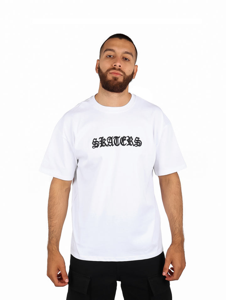 Hombre vistiendo playera blanca de manga corta con el texto SKATERS en letras negras.