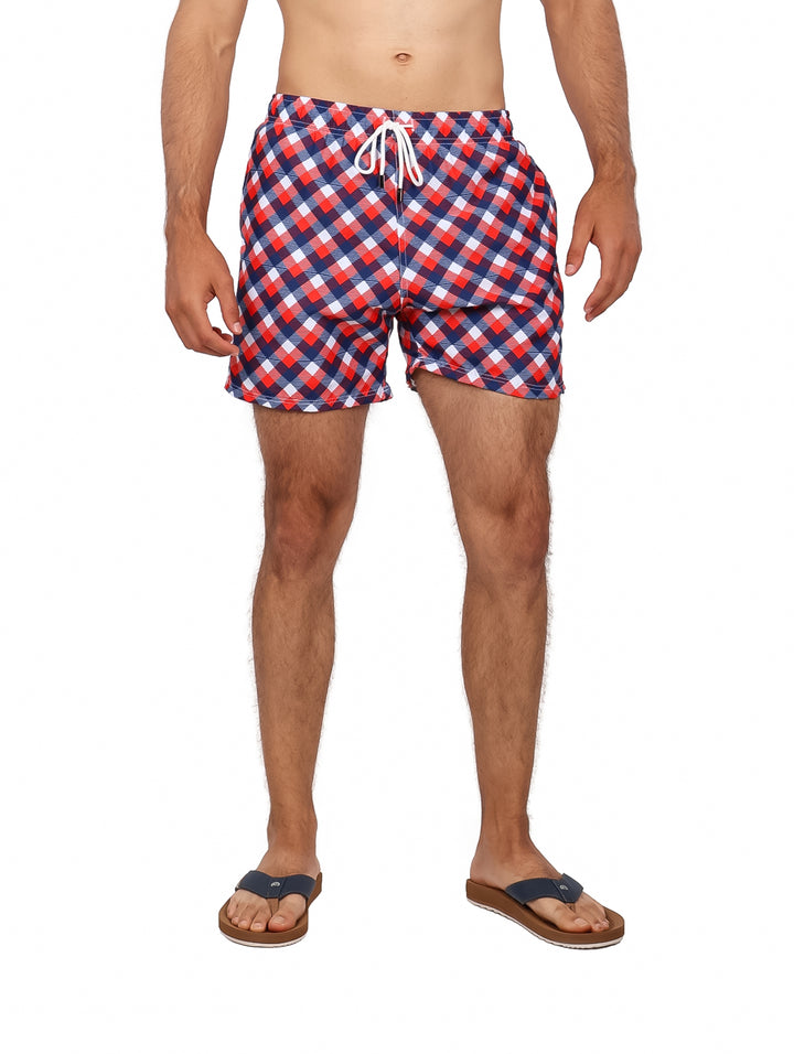 Hombre usando traje de baño corto con estampado de cuadros en colores rojo, azul y blanco.