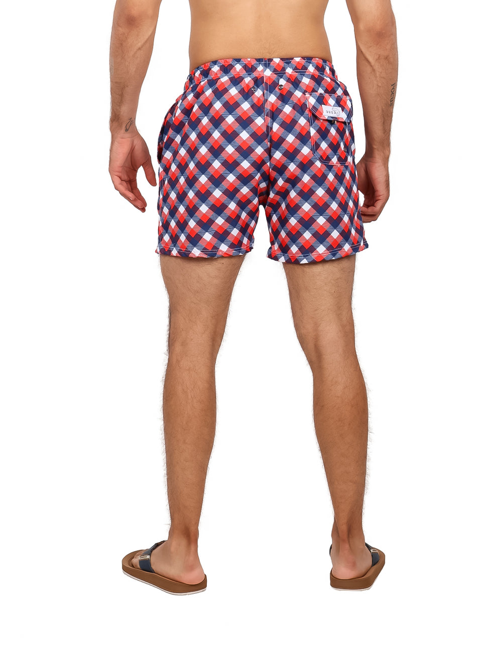 Hombre usando traje de baño corto con estampado de cuadros en colores rojo, azul y blanco.