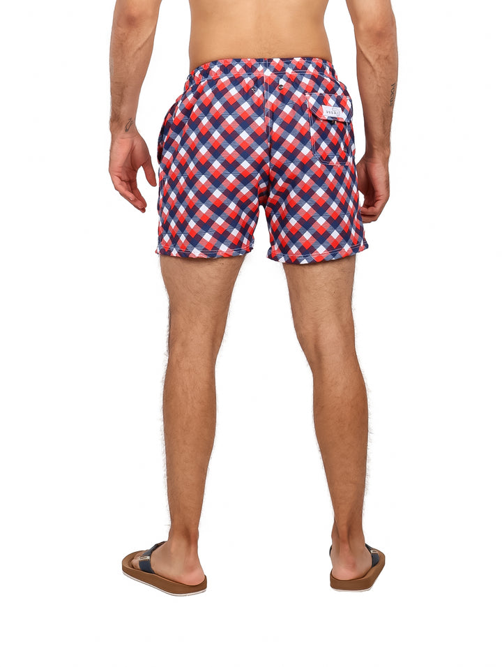 Hombre usando traje de baño corto con estampado de cuadros en colores rojo, azul y blanco.