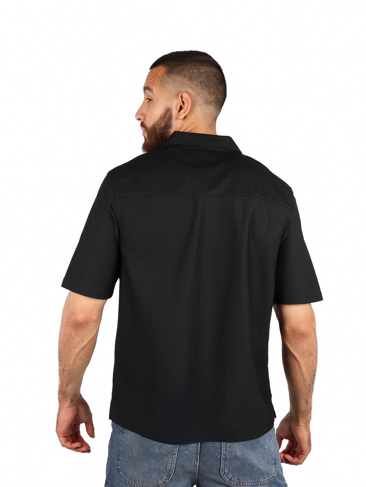 Hombre vistiendo una camisa negra de manga corta con botones y cuello.