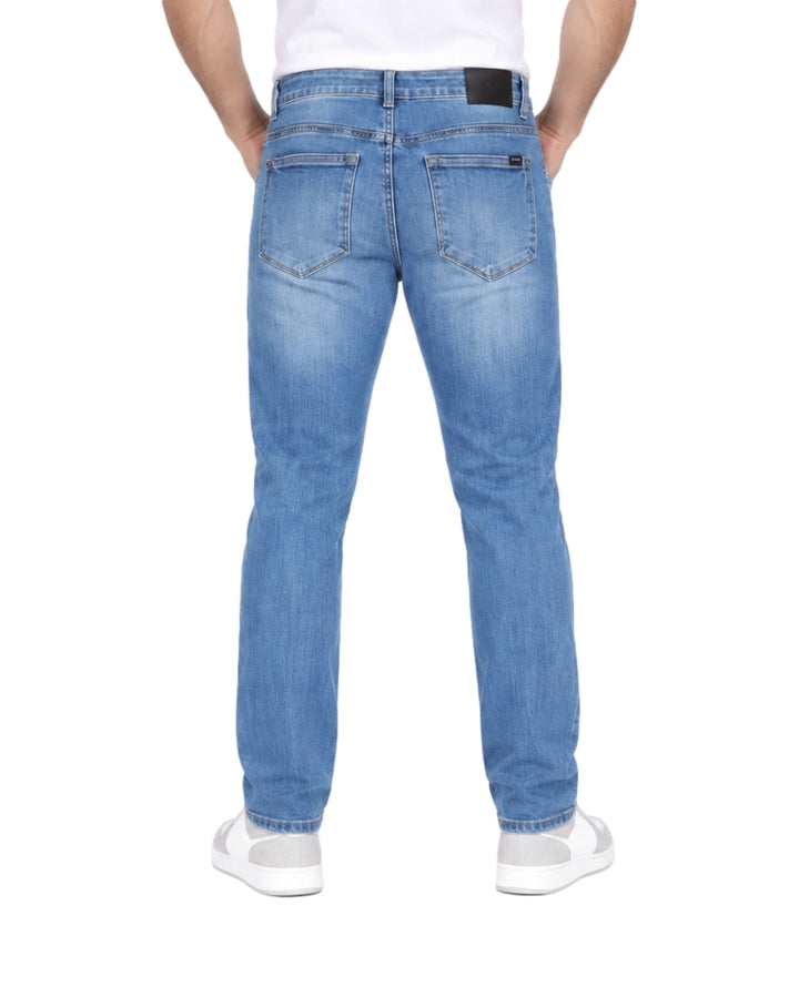 Hombre vistiendo jeans azul medio stone con detalles desgastados y rotos en las piernas.